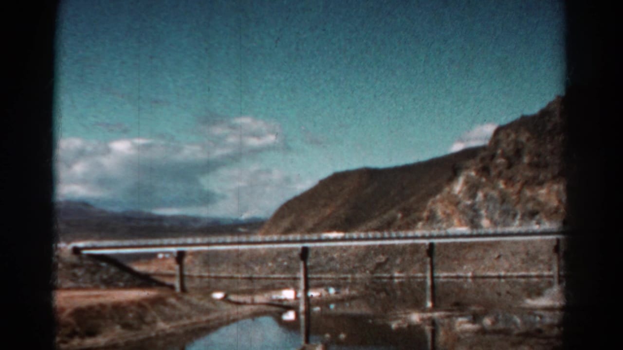 Bridge and concrete piers seen across water with hills in the background.