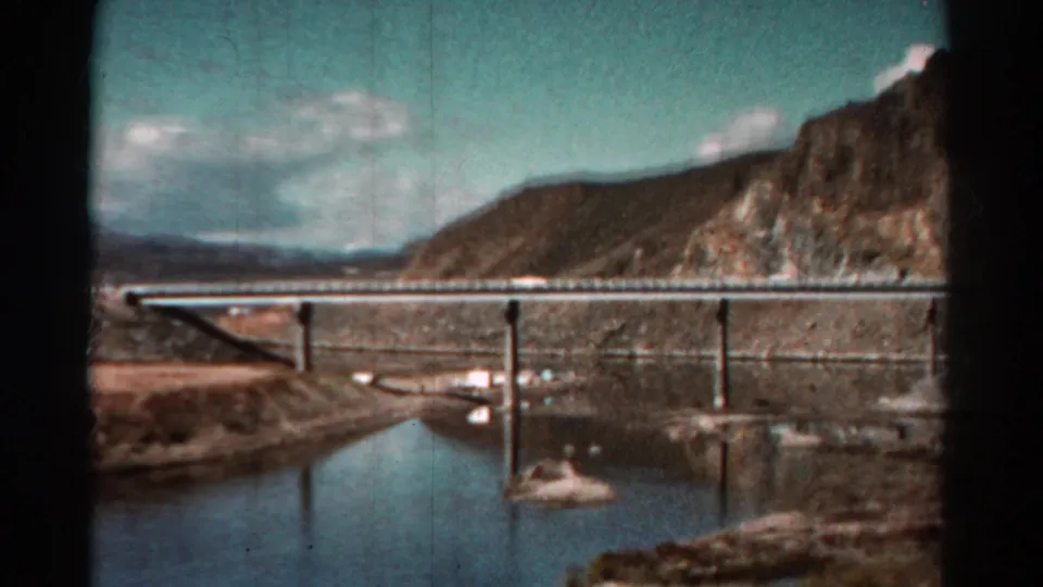 1967 Colorado 8mm frame showing bridge supports reflected in water, with a rocky shoreline and hills beyond.