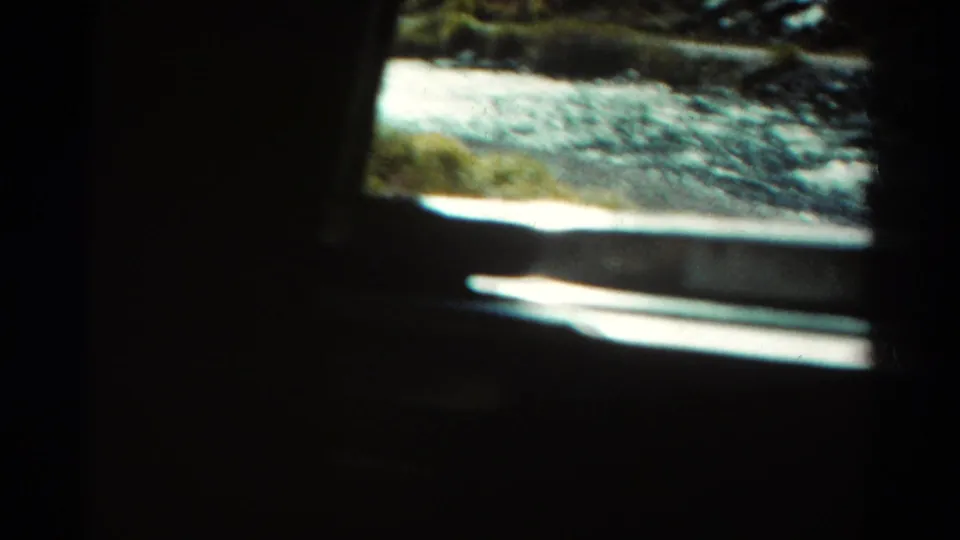 1967 Colorado roadside view where bright river water and shoreline appear partly obscured by a dark vehicle interior or window frame.