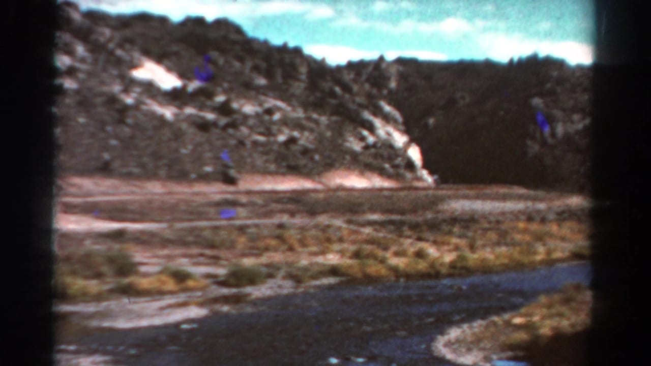 1967 Colorado 8mm frame showing a rocky mountain valley with a winding river, dry vegetation, dark tree slopes, and bright sky.