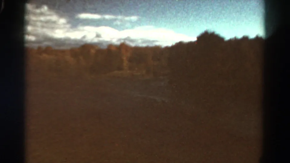 1967 Colorado 8mm landscape frame showing open terrain, autumn-toned trees, distant mountains or ridge, and a bright cloud bank.