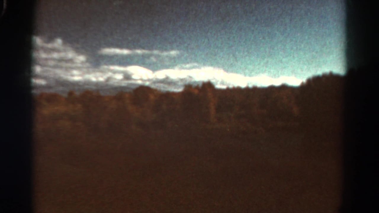 Snowy mountain ridge and treeline across open countryside with dark film-edge borders.