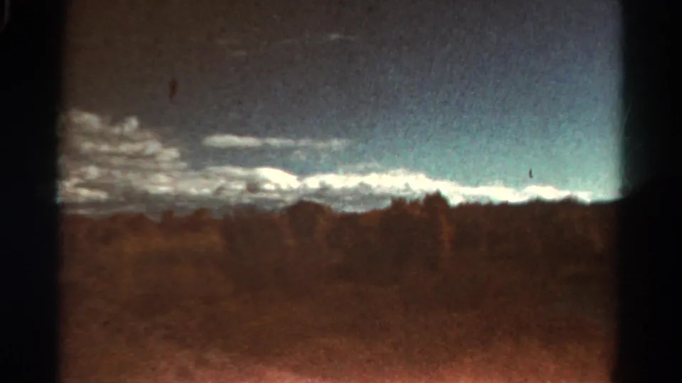 Grainy 1967 Colorado frame with distant mountains, a dark wooded horizon, open brown land, and visible film wear at the frame edges.
