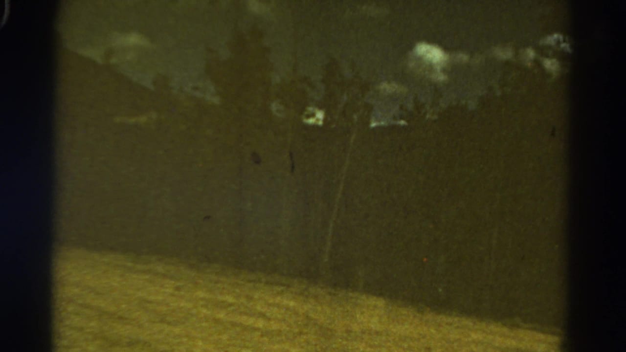 Soft roadside landscape with field, trees, clouds, and dark film borders.
