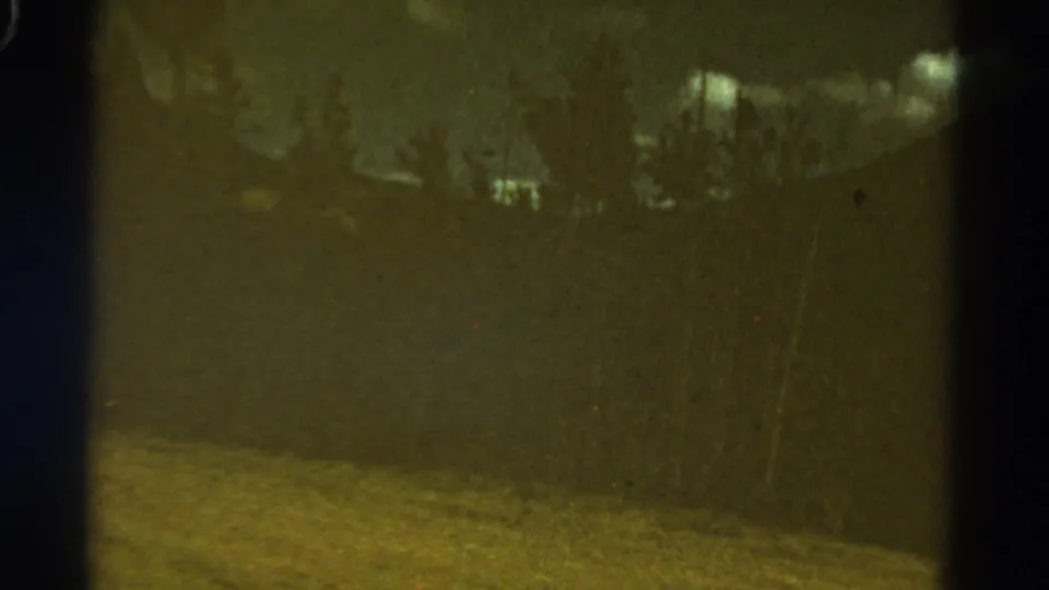 1967 Colorado travel footage frame with a blurred field, trees, cloudy sky, and visible 8mm frame wear.