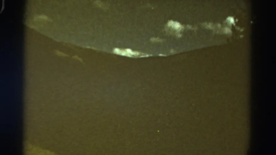 1967 Colorado home-movie frame showing a faded mountain ridge, dark foreground, and low cloudy sky.