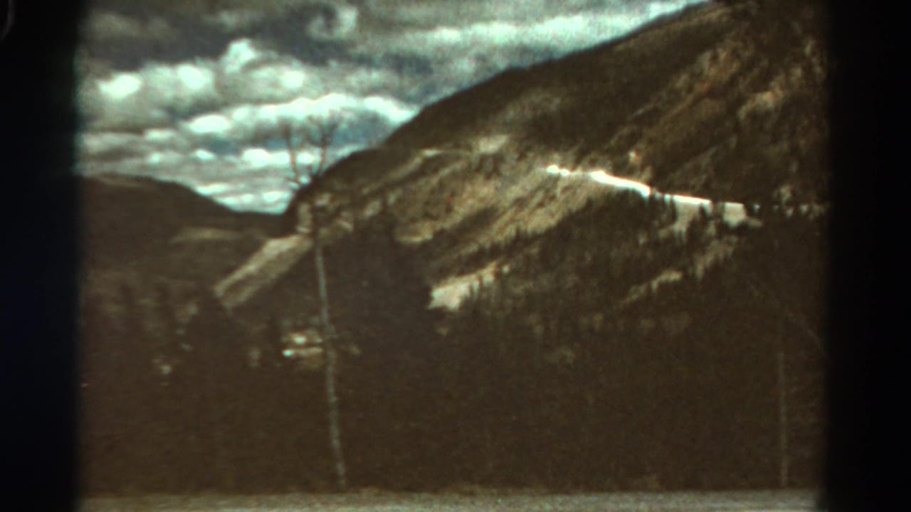 1967 Colorado 8mm frame with a bright road line across a rugged mountainside and heavy clouds overhead.