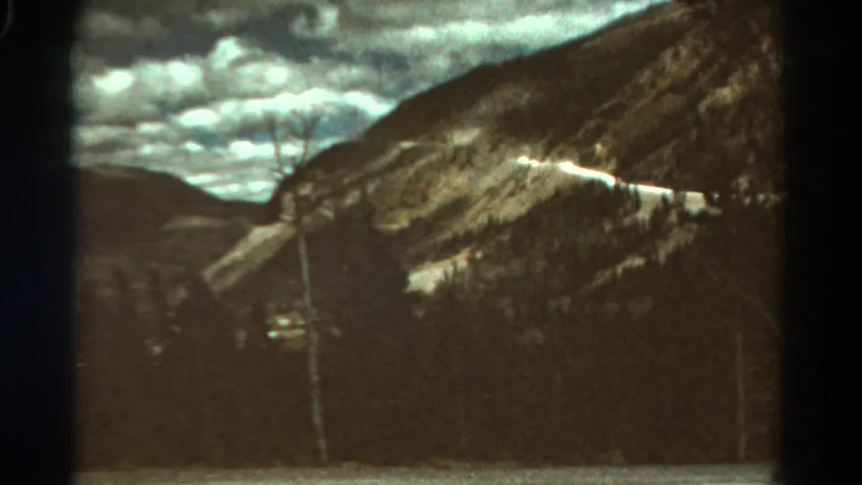 1967 Colorado 8mm frame with a bright road line across a rugged mountainside and heavy clouds overhead.