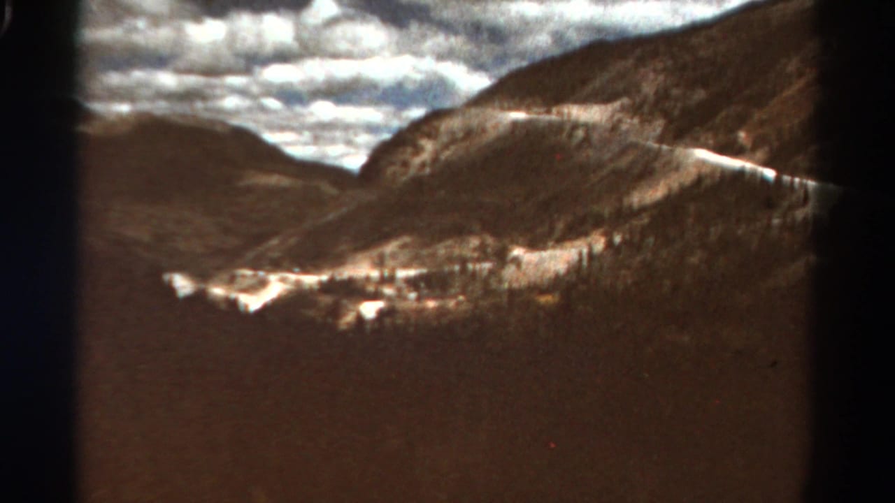 Sunlit mountain slopes and valley with bright cloud cover and a pale line across the hillside.