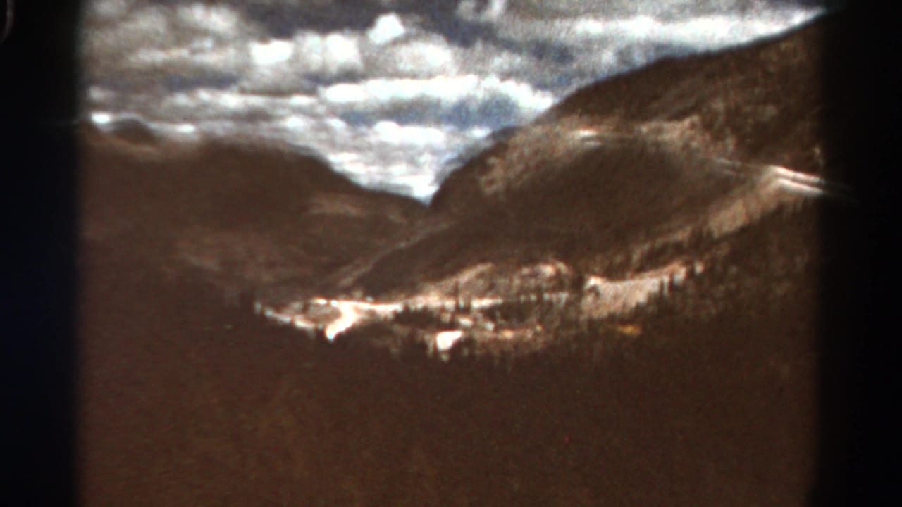 Dark mountain valley beneath bright broken clouds on aged color film.