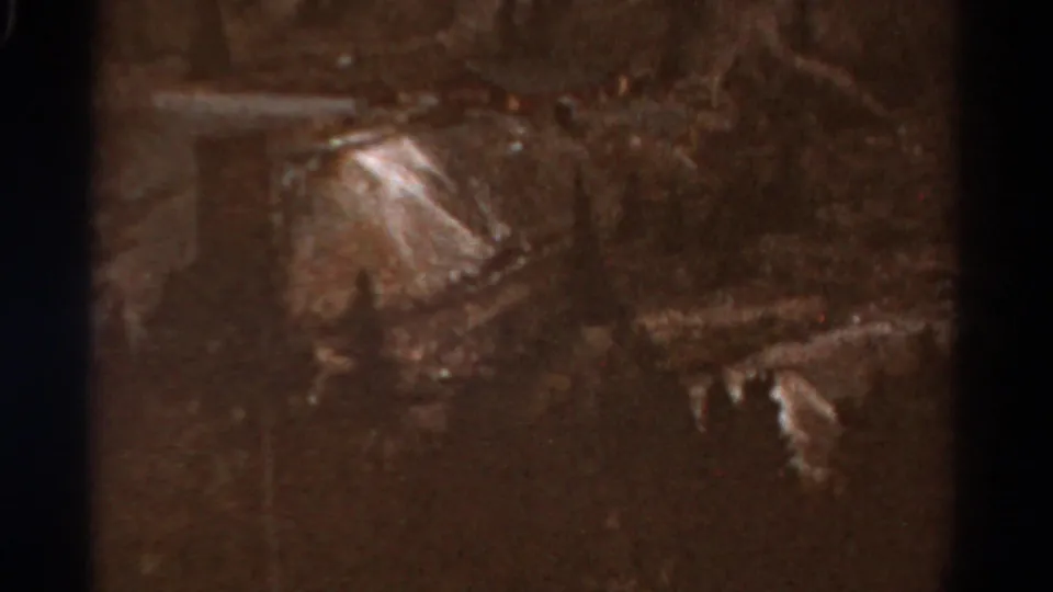 1967 Colorado 8mm frame looking down into a dim valley with sloping terrain, pale ground patches, and heavy home-movie grain.