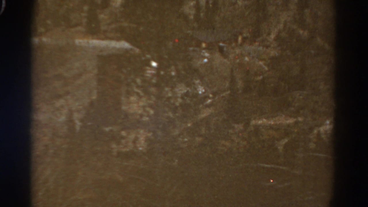 1967 Colorado home-movie frame with a dim view of a cut hillside or rough road area, softened by grain and exposure variation.