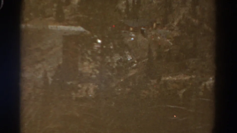 1967 Colorado home-movie frame with a dim view of a cut hillside or rough road area, softened by grain and exposure variation.