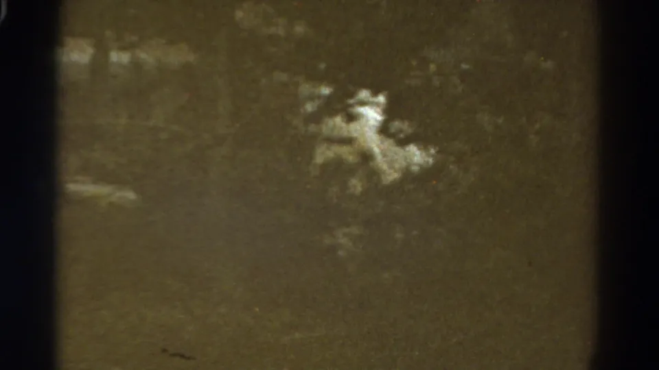 Grainy 1967 Colorado road footage shows dark vegetation and a pale central form, likely part of the hillside or roadside scene.