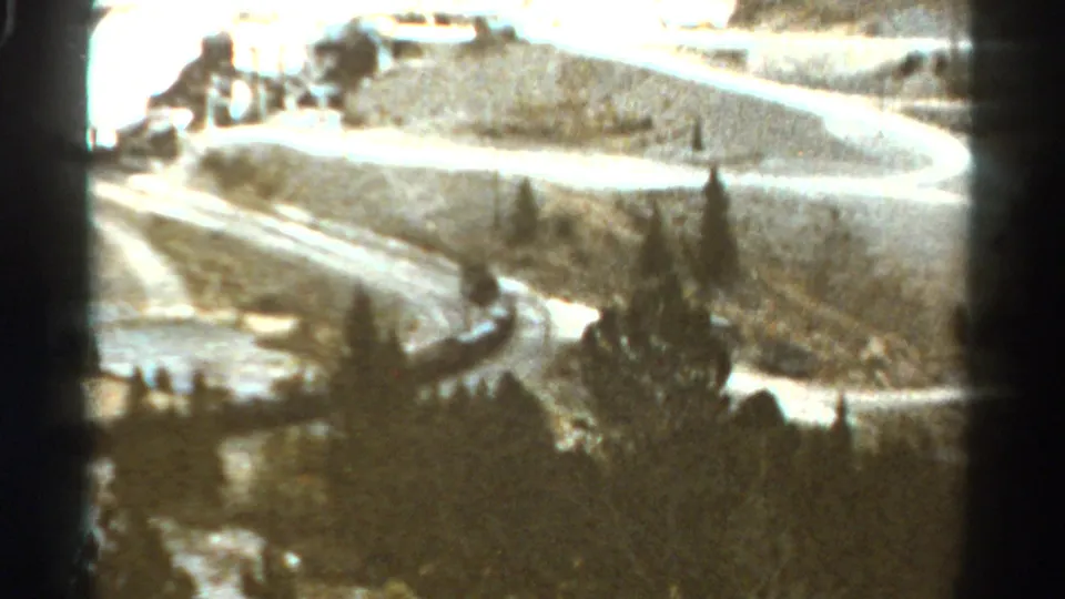 1967 Colorado 8mm frame showing a winding hillside road, pine trees, and a small dark vehicle-like shape near the curve.