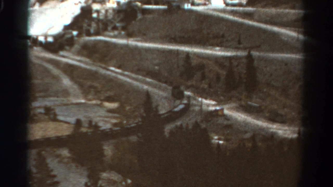 A distant passenger train follows a winding Colorado mountain track, framed by soft 8mm grain and dark film edges.