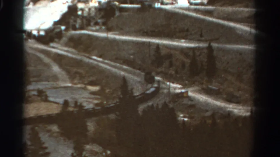 A distant passenger train follows a winding Colorado mountain track, framed by soft 8mm grain and dark film edges.