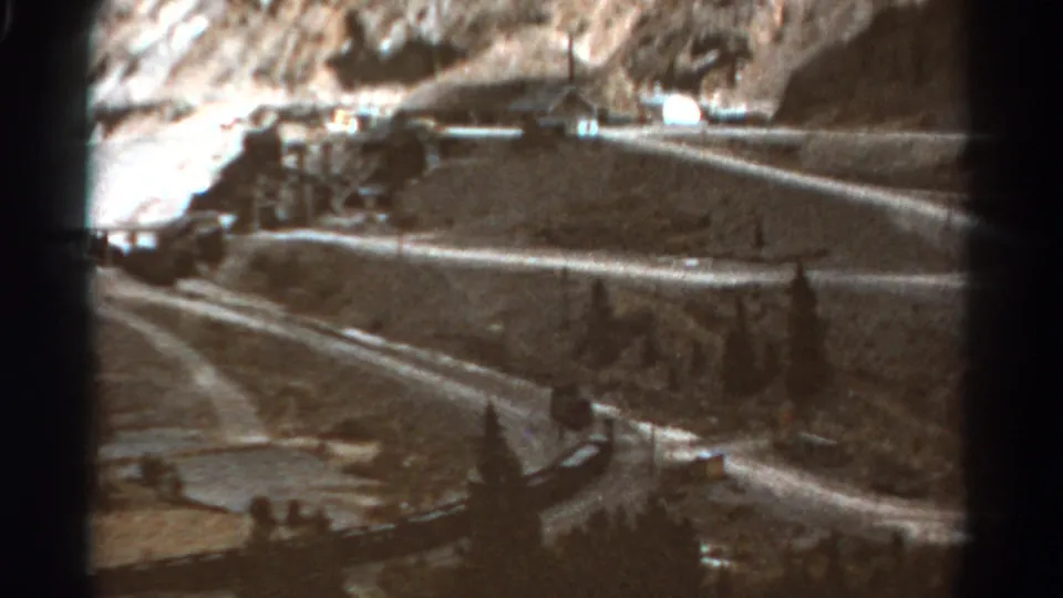 1967 Colorado footage shows a passenger train curving through a mountain landscape with trees, road-like lines, and rocky ground.