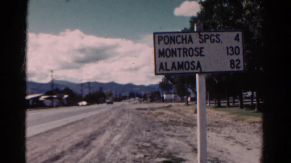 1967 Colorado roadside frame showing the Poncha Spgs., Montrose, and Alamosa distance sign near a two-lane road under a cloudy sky.