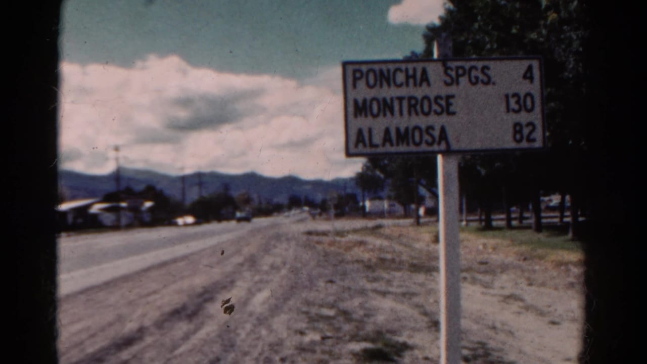 1967 Colorado 8mm frame showing a distance sign for Poncha Springs, Montrose, and Alamosa beside a quiet road.