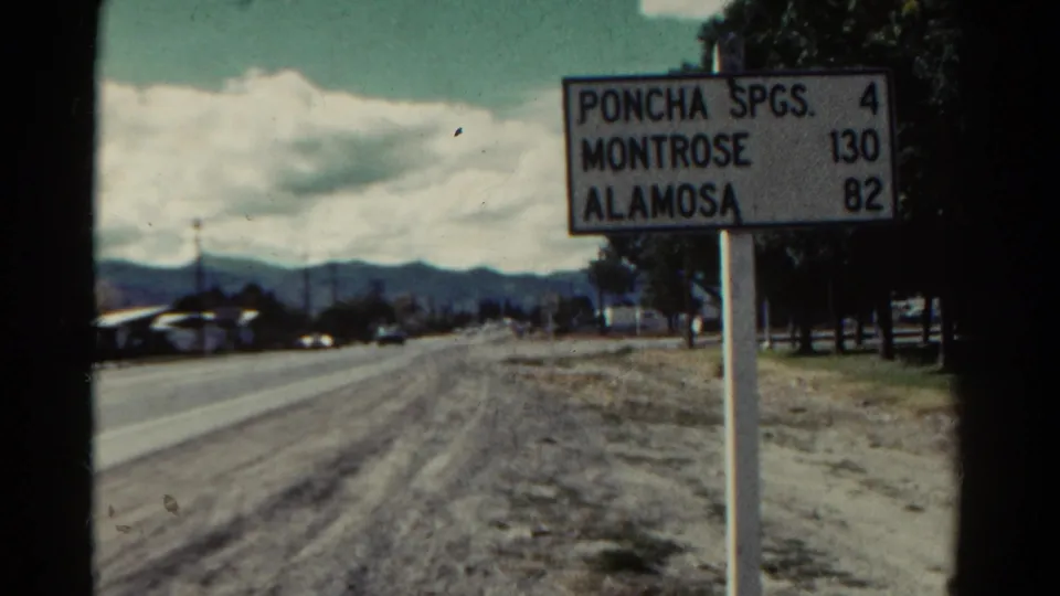1967 Colorado 8mm frame showing the Poncha Springs, Montrose, and Alamosa mileage sign beside a rural route.