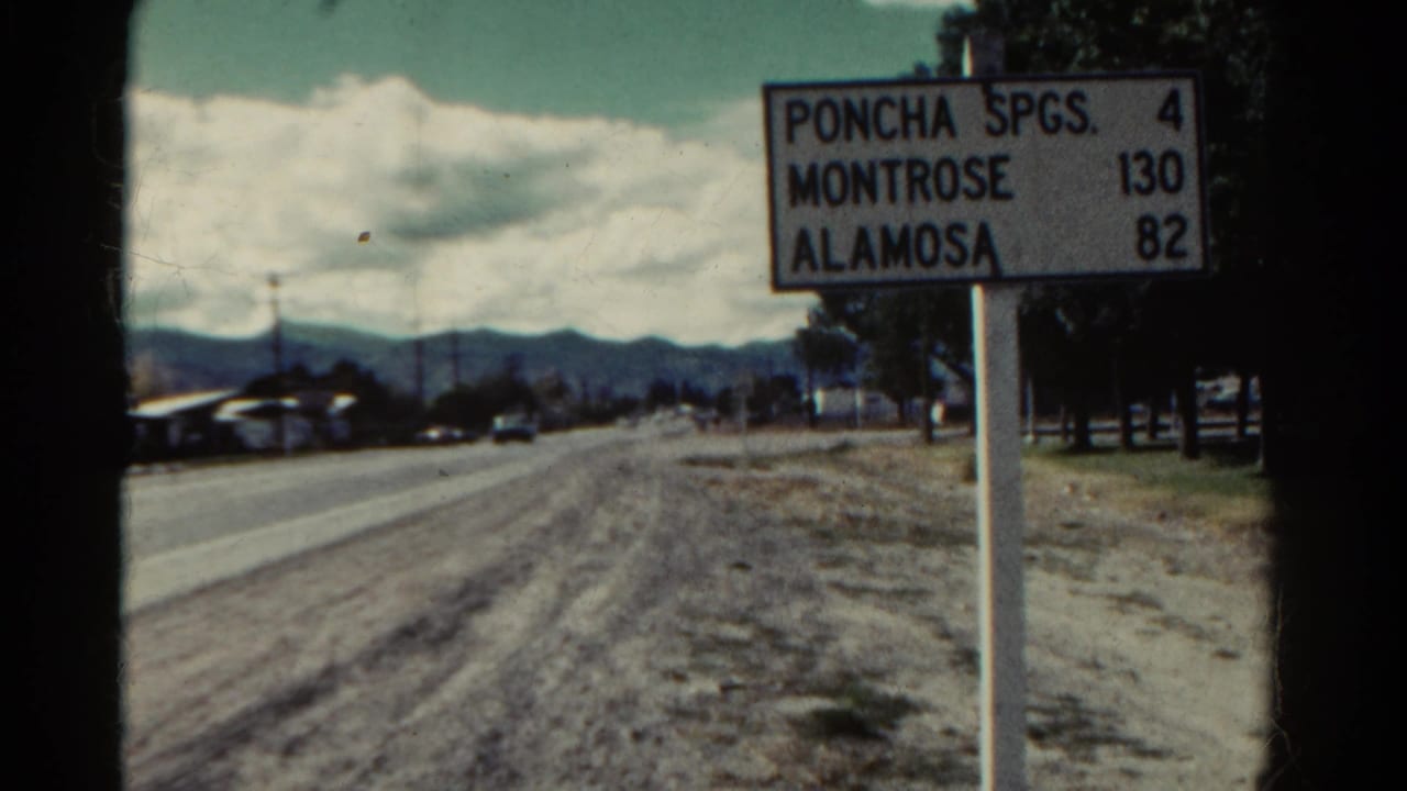 1967 Colorado home-movie frame showing a roadside sign for Poncha Springs, Montrose and Alamosa beside a rural road.