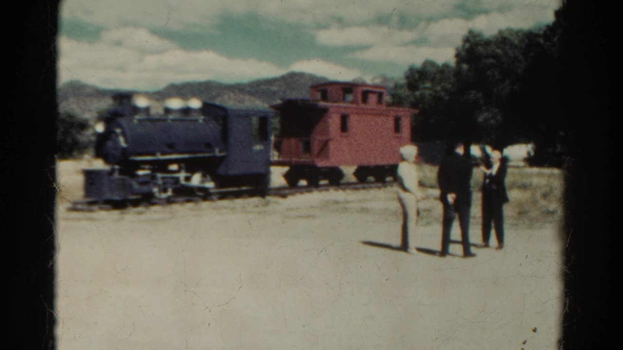 1967 Colorado frame with three visitors facing a stationary dark locomotive and red caboose under a partly cloudy sky.