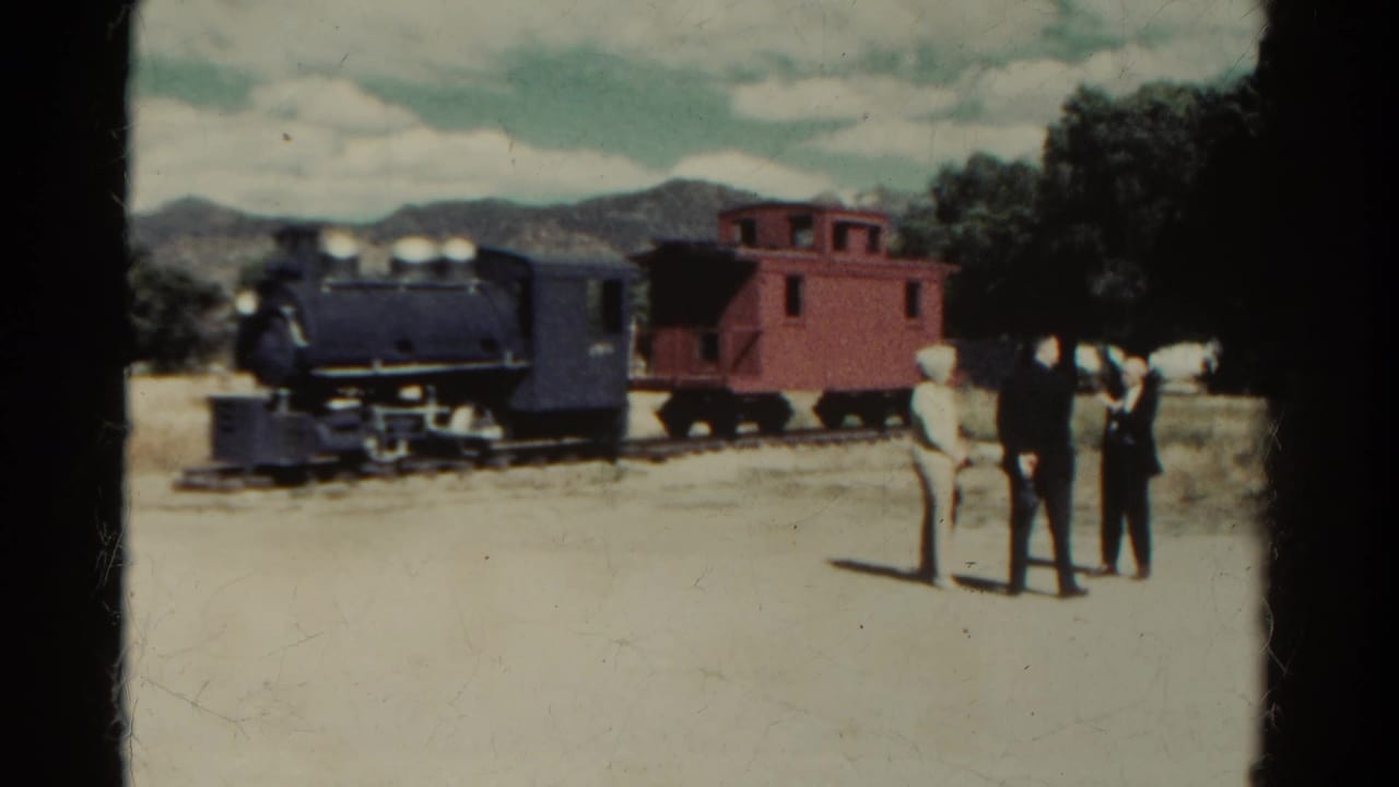 1967 Colorado 8mm frame showing three adults near a stationary steam locomotive and red caboose in a mountain setting.