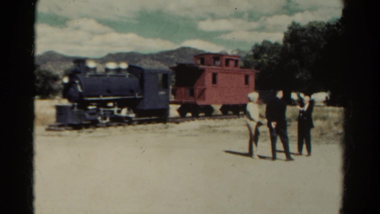 1967 Colorado home-movie frame with three adults beside a steam locomotive, red caboose, trees, and distant mountains.