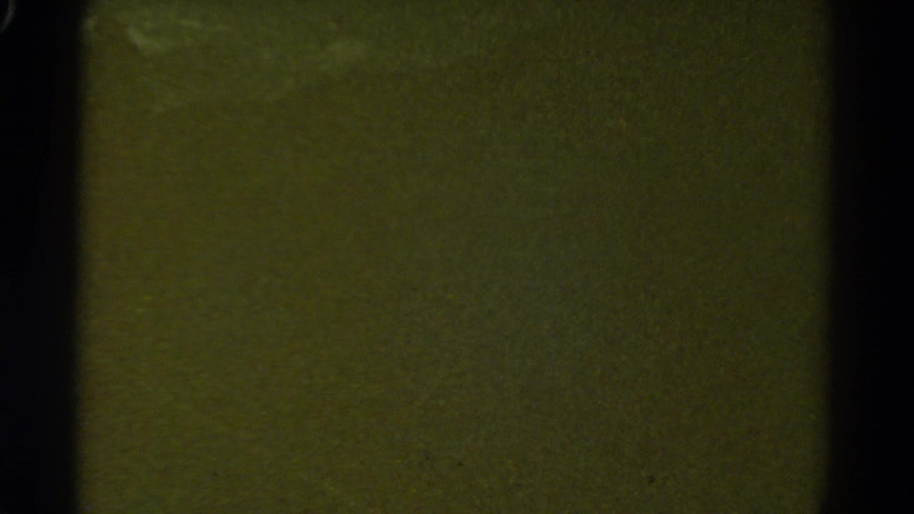 Green-tinted 8mm leader or transitional dark frame with vertical frame-edge shadow and no clear train detail visible.