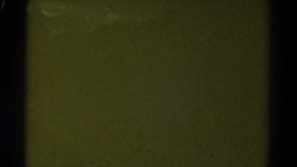Green-tinted 8mm leader or transitional dark frame with vertical frame-edge shadow and no clear train detail visible.