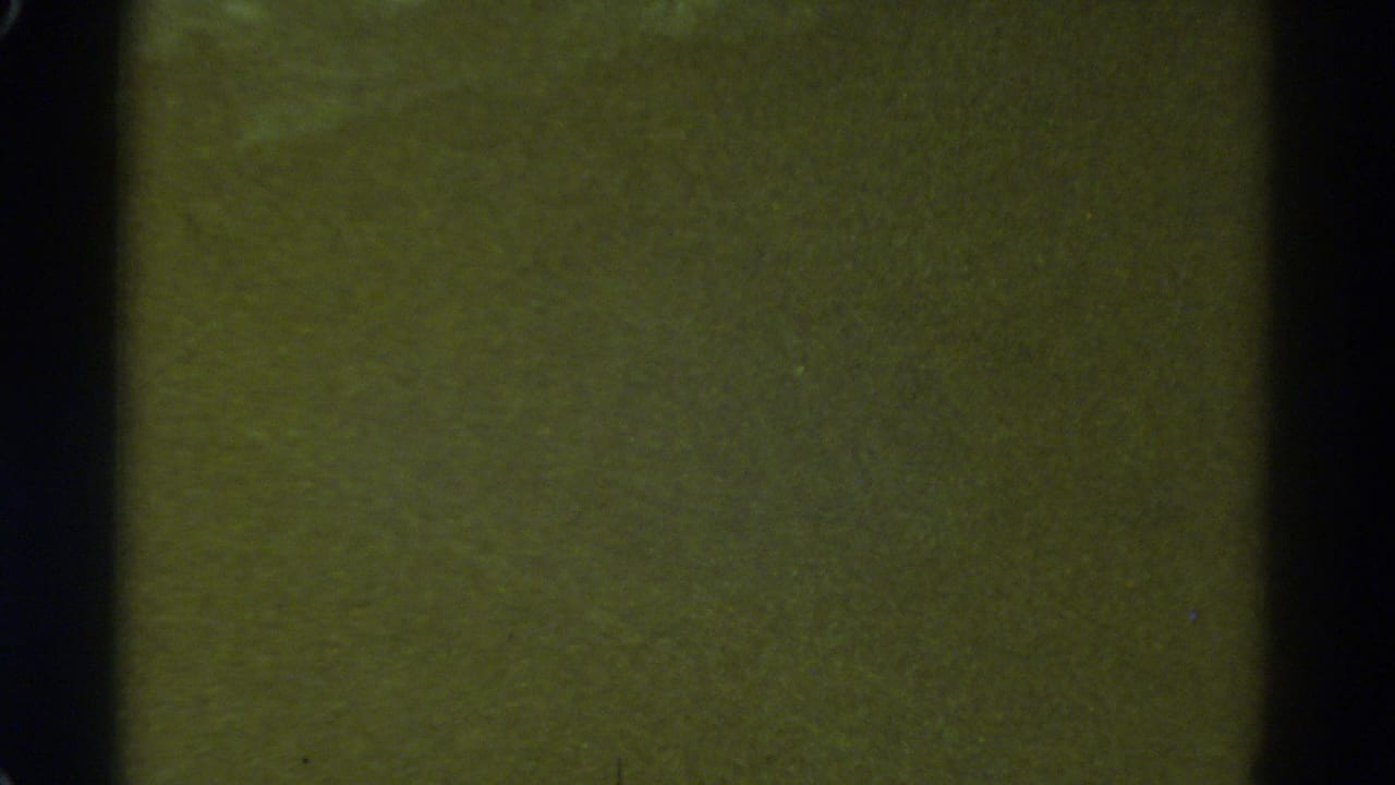 1967 Colorado home-movie frame showing a blurred green surface with heavy grain, scratches, and dark 8mm gate edges.