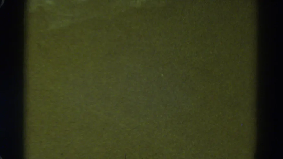1967 Colorado home-movie frame showing a blurred green surface with heavy grain, scratches, and dark 8mm gate edges.