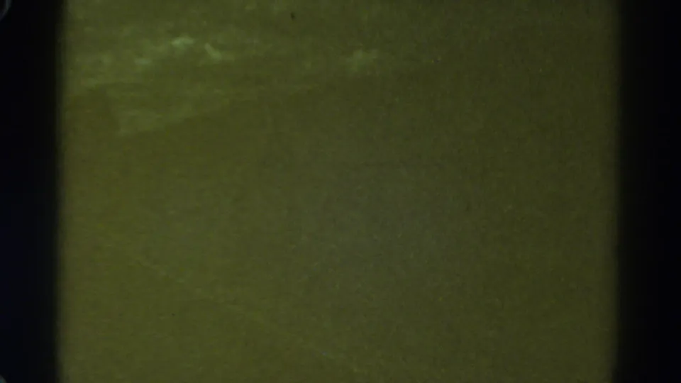 1967 Colorado 8mm home-movie frame with out-of-focus green texture, dark borders, dust, scratches, and muted exposure.
