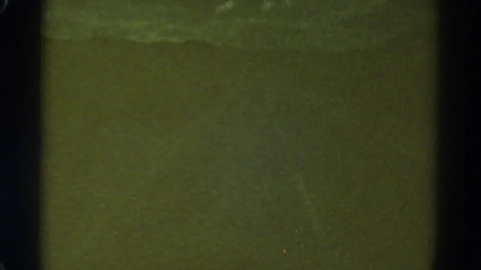 1967 Colorado 8mm night-driving frame with mostly dark green exposure, black gate edges, and scattered film specks.