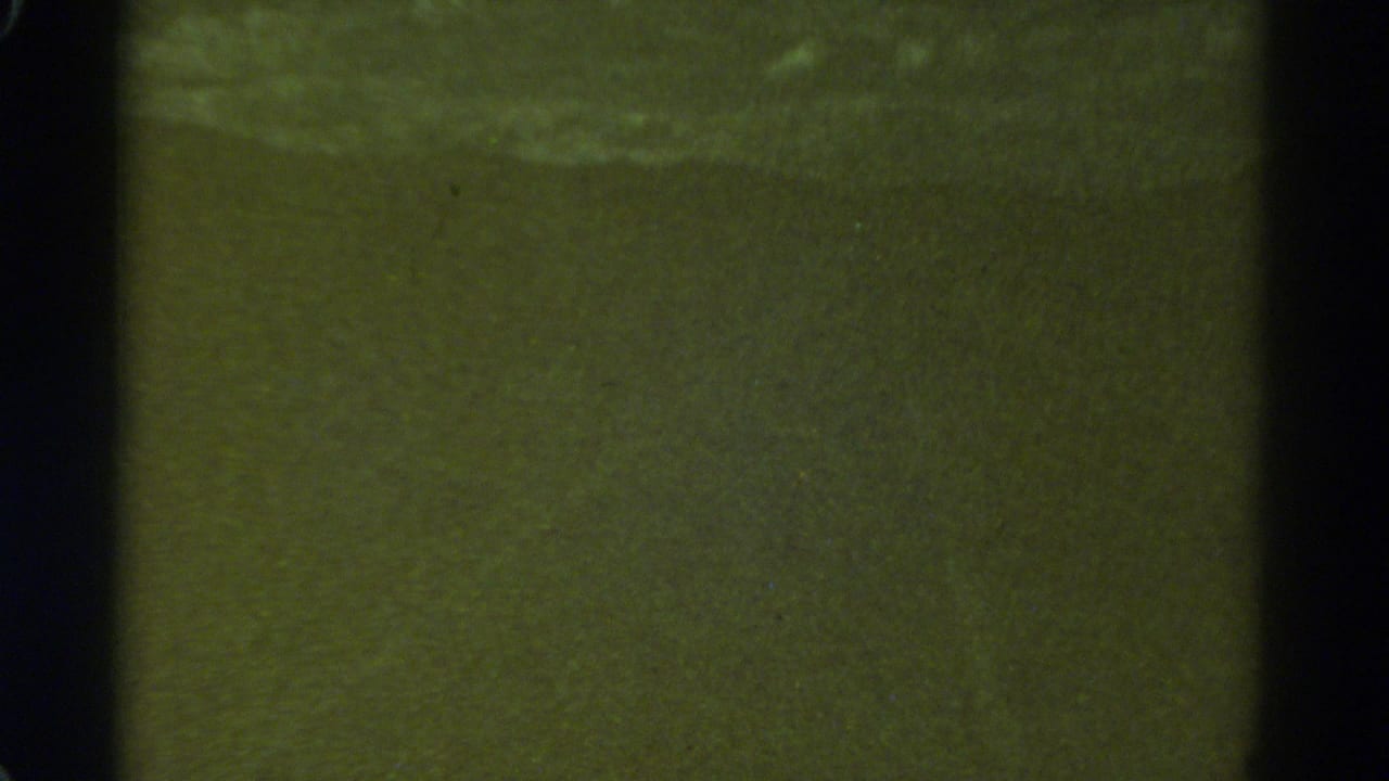 1967 Colorado home-movie frame showing a low-light night road view reduced to greenish tone, grain, and gate-edge shadows.