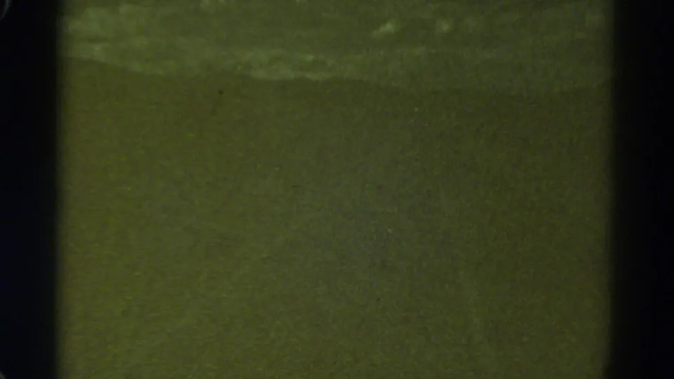 1967 Colorado home-movie frame showing a low-light night road view reduced to greenish tone, grain, and gate-edge shadows.