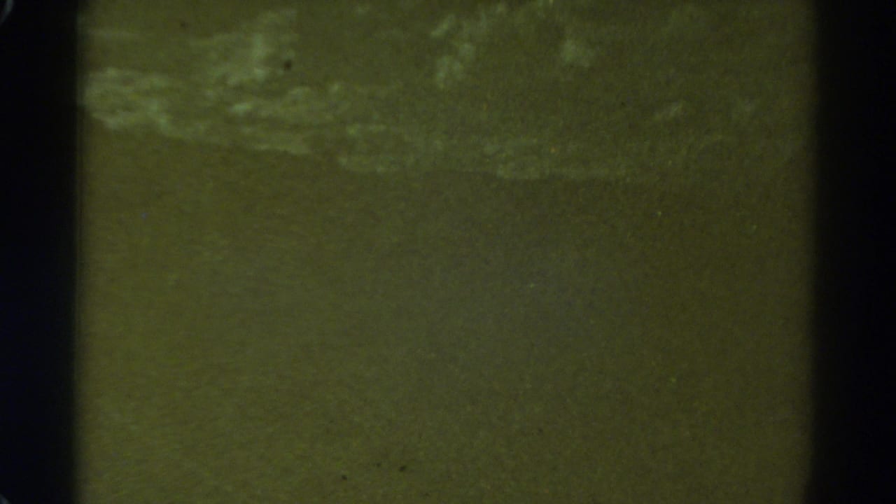 Greenish grainy surface with pale wave-like streaks and dark film edges.