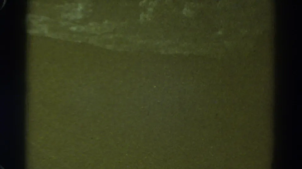 Indistinct 1967 8mm frame showing a greenish water or shore texture with pale movement near the upper area.