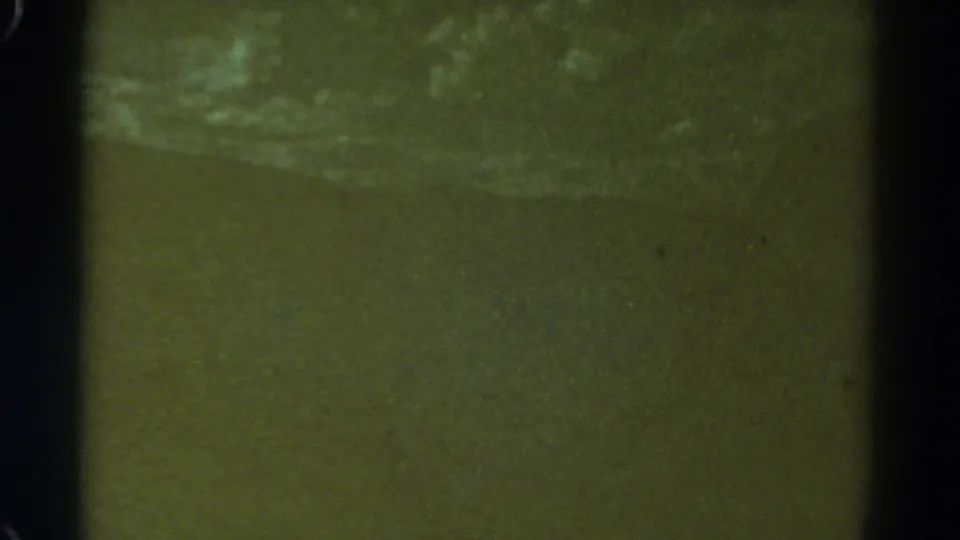 1967 8mm frame from supplied metadata, with brighter pale marks suggesting distant water movement on a greenish surface.