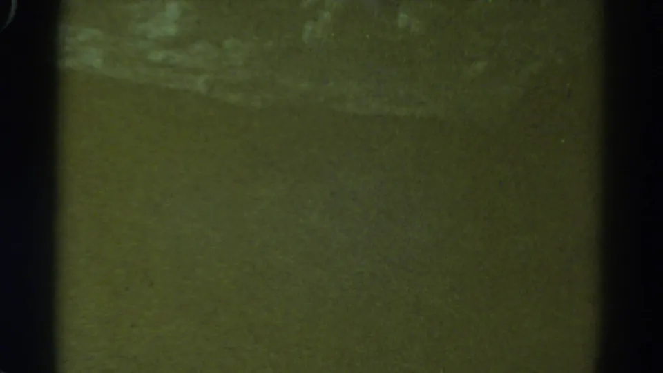 Soft 1967 8mm frame showing indistinct greenish shoreline or water texture, with pale bands and visible aging marks.