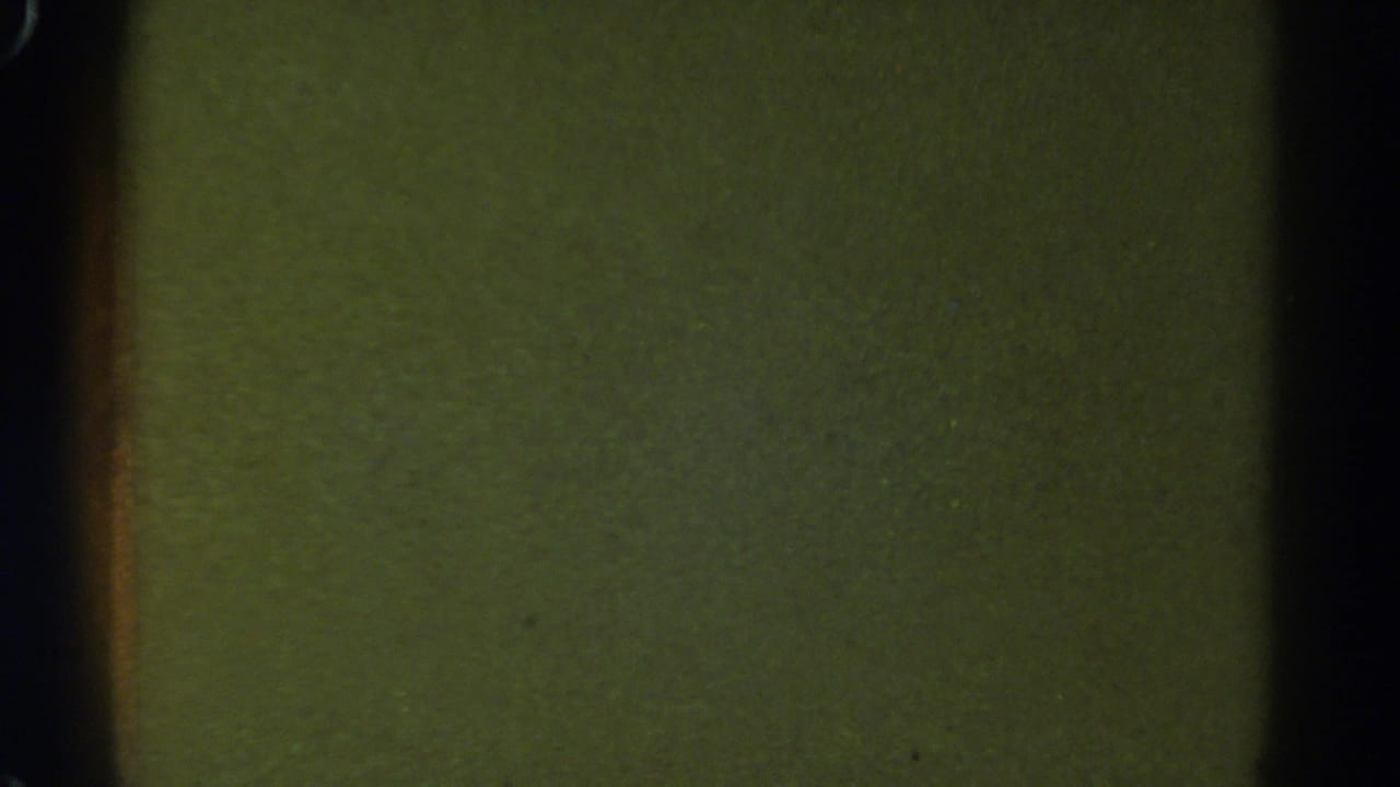 1967 Colorado 8mm frame showing a blank green-yellow film field with dark edge shadows, grain, and small specks.