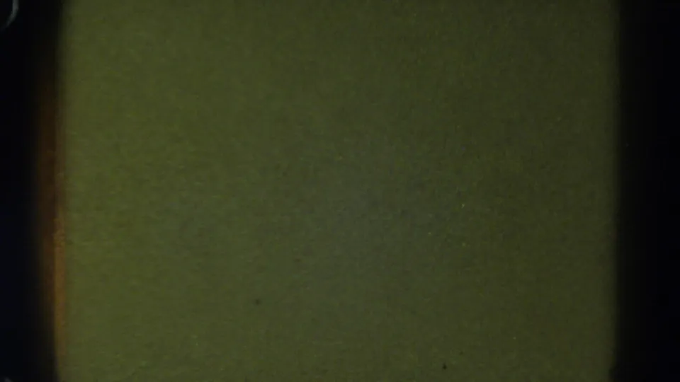 1967 Colorado 8mm frame showing a blank green-yellow film field with dark edge shadows, grain, and small specks.