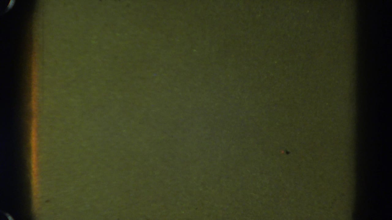 1967 Colorado 8mm frame with a greenish blank field, dark vertical gate shadow, faint specks, and soft film texture.