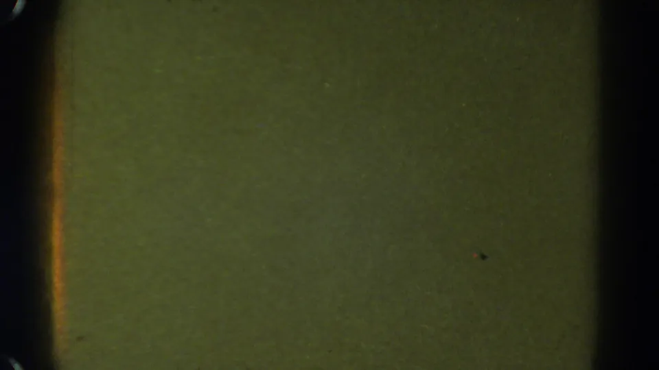 1967 Colorado 8mm frame with a greenish blank field, dark vertical gate shadow, faint specks, and soft film texture.