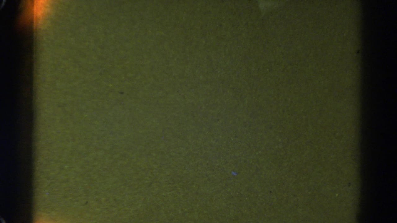 1967 Colorado 8mm frame showing a mostly dark, greenish road or night scene with faint orange glow along the left edge.