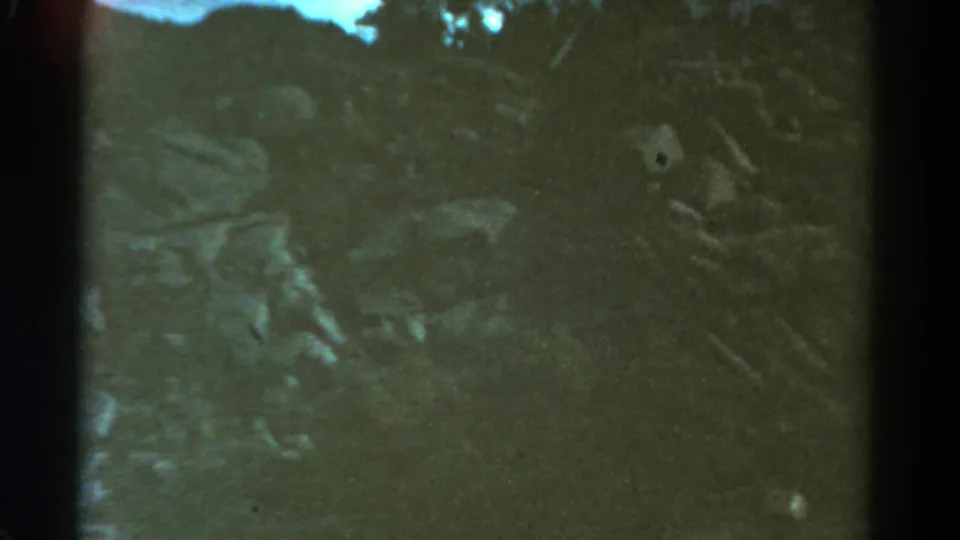 Dark 8mm view of Colorado mountain terrain, with rocks, brush, and pale sky visible through heavy grain and soft focus.