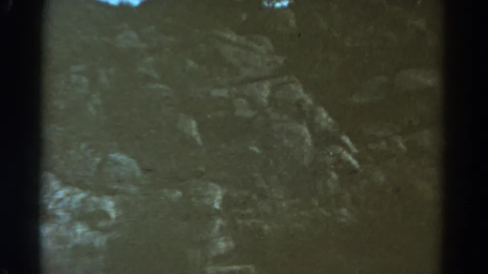 1967 Colorado travel footage shows a dim, green-shifted view of rocky ground and brush, likely seen from a moving train.