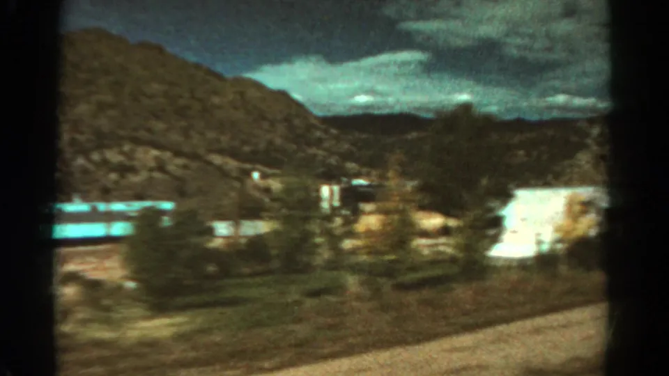1967 Colorado 8mm frame with motion blur across trees, low buildings, mountain ridges, and clouds.