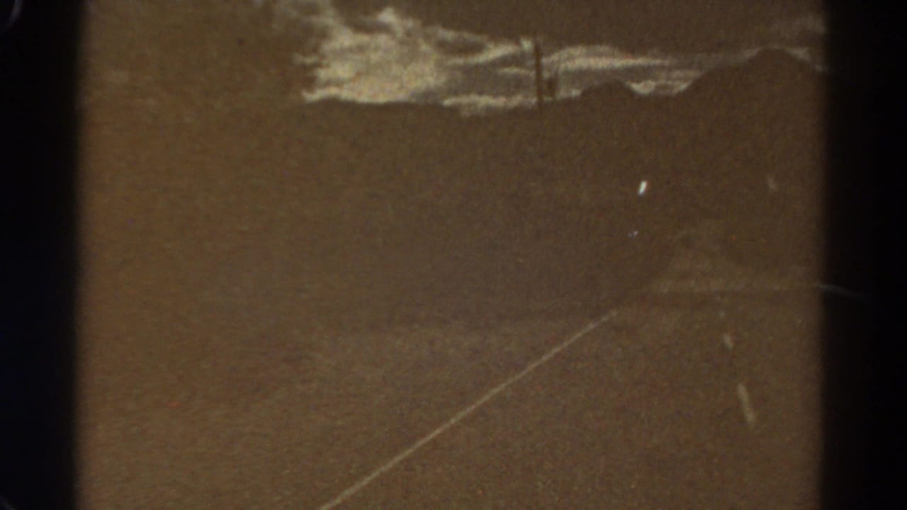 Empty asphalt road with a pale center line, distant ridgeline, cloudy sky and film scratches.